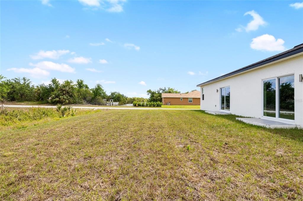 The exterior of a white house features a grassy backyard overlooking a canal and trees — 10026 COCOA BEACH STREET, PORT CHARLOTTE, FL