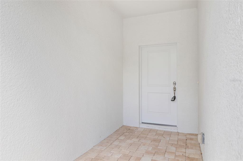 A white door with a lockbox opens onto a small, paved entryway with textured walls — 10026 COCOA BEACH STREET, PORT CHARLOTTE, FL