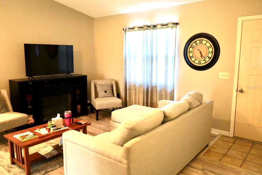 A living room features a television on a console, a sofa, an armchair, and a wall clock — 10046 CHARLEMONT AVENUE, ENGLEWOOD, FL