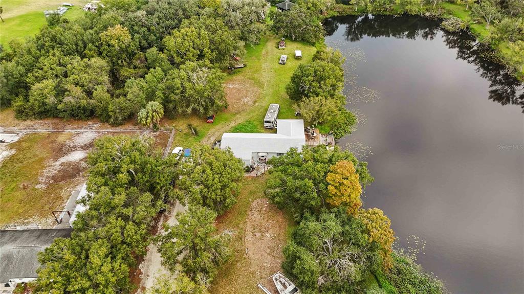 An aerial view shows a house with a white roof situated beside a large pond — 8011 41ST AVENUE E, BRADENTON, FL