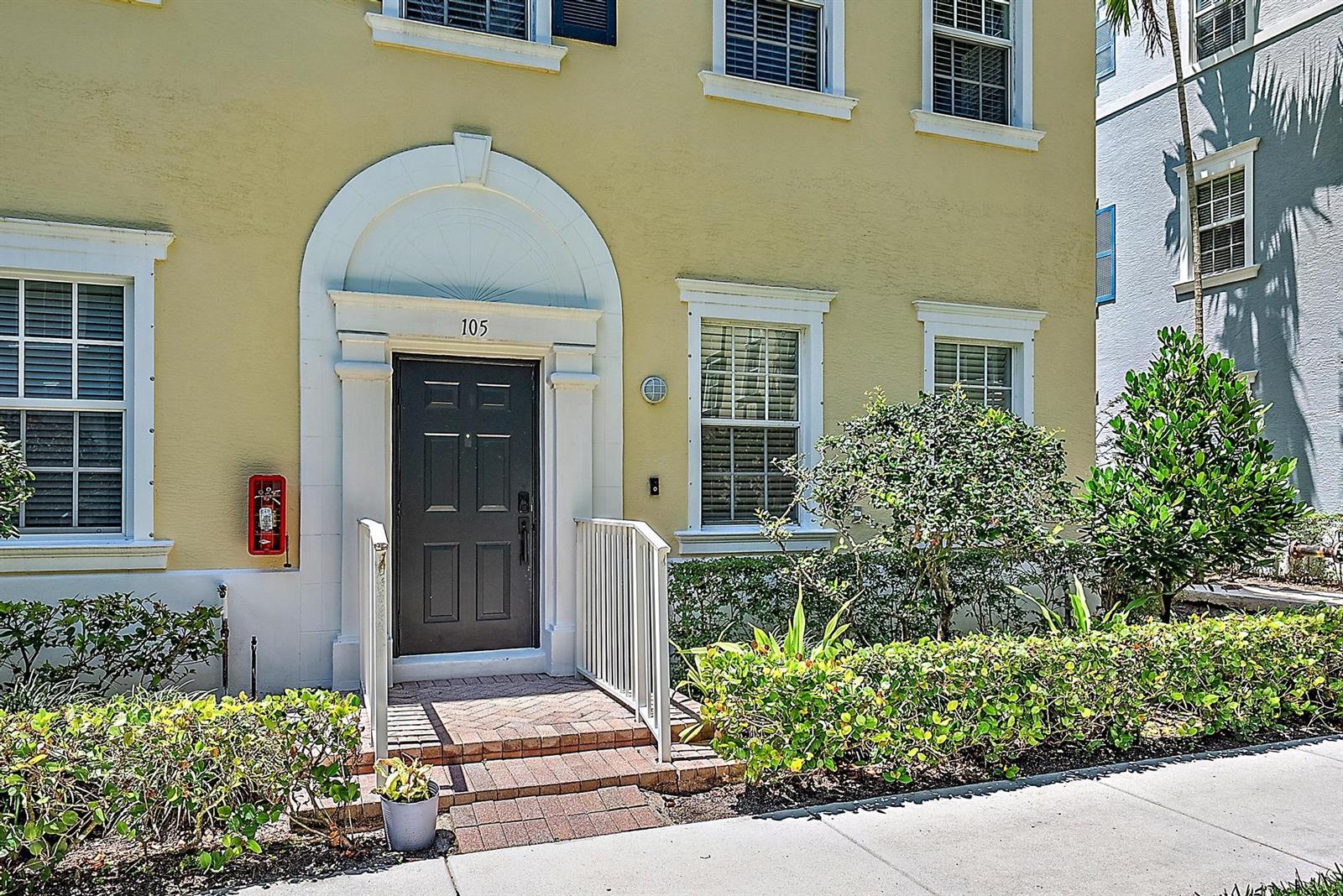 A yellow building exterior features a dark front door with a white arched entryway — 107 Pond Apple Lane # 105, Jupiter FL 33458, JUPITER, FL