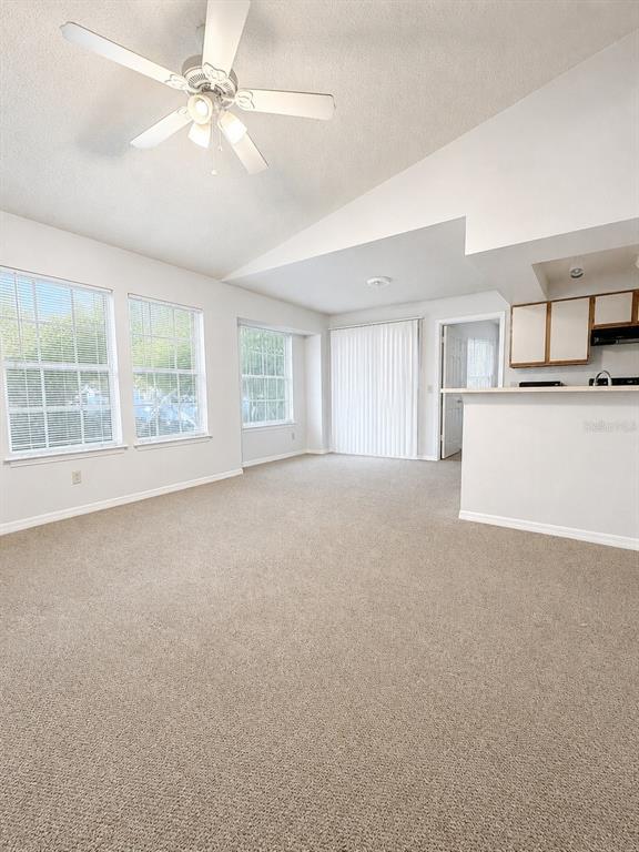 A living room with beige carpet, a ceiling fan, and a kitchen breakfast bar — 1033 S HIAWASSEE ROAD UNIT 2622, ORLANDO, FL