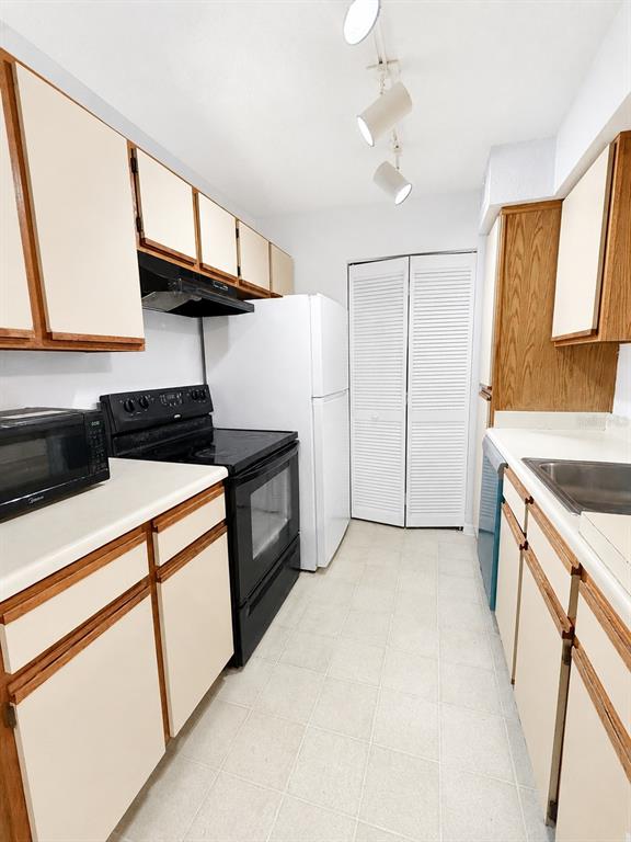 A galley kitchen features white cabinets with wood trim, black appliances, and white tile flooring — 1033 S HIAWASSEE ROAD UNIT 2622, ORLANDO, FL