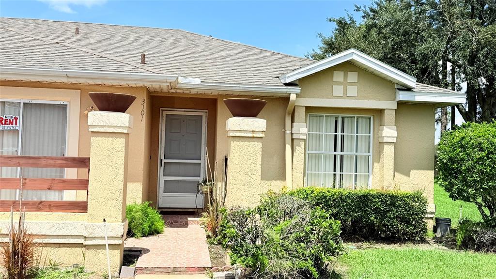 The exterior of a tan, single-story house features a front entrance and a small yard — 3101 TADPOLE COURT, KISSIMMEE, FL