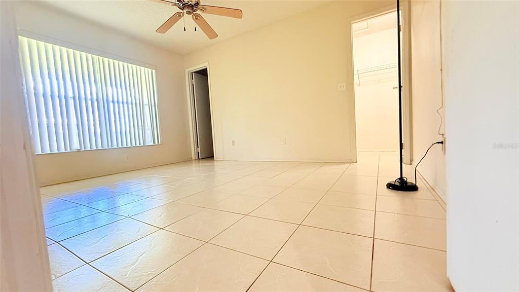 An empty room features light-colored floor tiles, a ceiling fan, and vertical window blinds — 3101 TADPOLE COURT, KISSIMMEE, FL