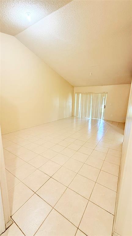 An empty room with light-colored tile flooring, a vaulted ceiling, and sliding glass doors — 3101 TADPOLE COURT, KISSIMMEE, FL