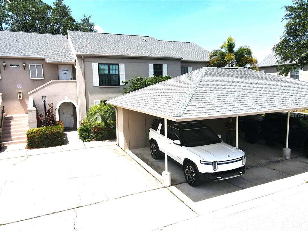 A white SUV is parked under a carport next to a two-story residential building — 2480 PELICAN COURT UNIT 102R, CLEARWATER, FL