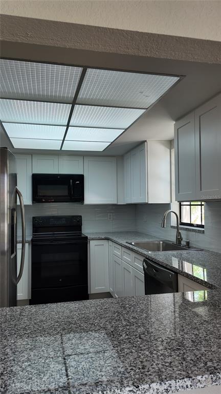 A kitchen features white cabinets, granite countertops, a black stove, and a recessed ceiling light — 2480 PELICAN COURT UNIT 102R, CLEARWATER, FL