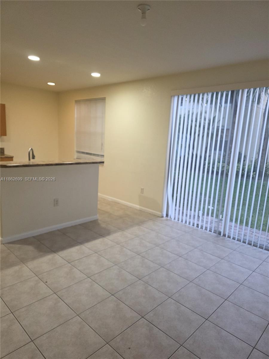 A room with light-colored tile flooring, a kitchen pass-through counter, and vertical sliding glass doors — 2584 SW 84th Ter # 101, Miramar FL 33025, MIRAMAR, FL