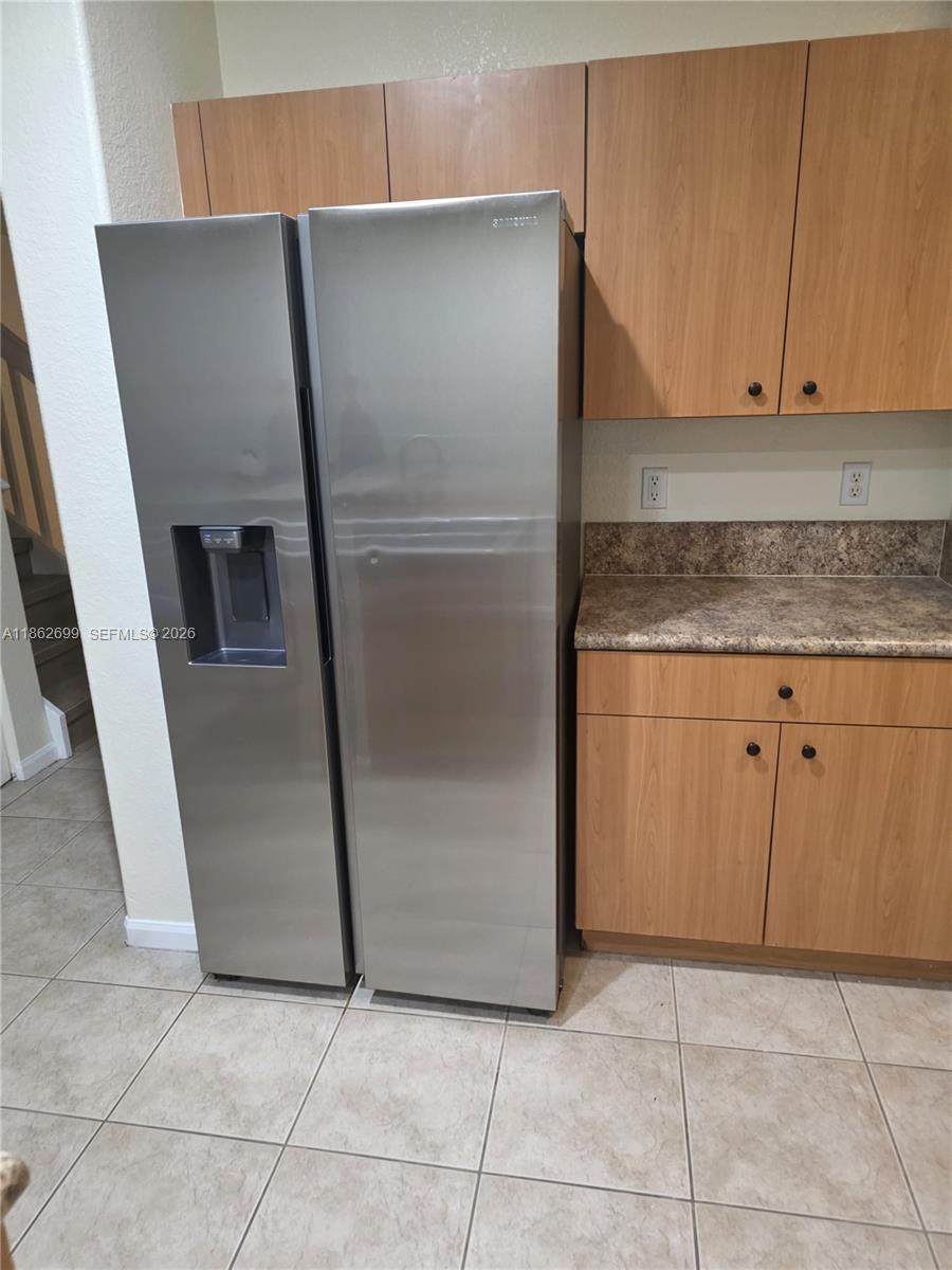 A stainless steel refrigerator stands next to wooden kitchen cabinets and a laminate countertop — 2584 SW 84th Ter # 101, Miramar FL 33025, MIRAMAR, FL