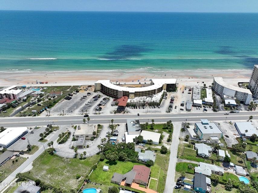 An aerial view shows a curved beachfront hotel with a parking lot and surrounding buildings — 2301 S ATLANTIC AVENUE UNIT 438, DAYTONA BEACH, FL