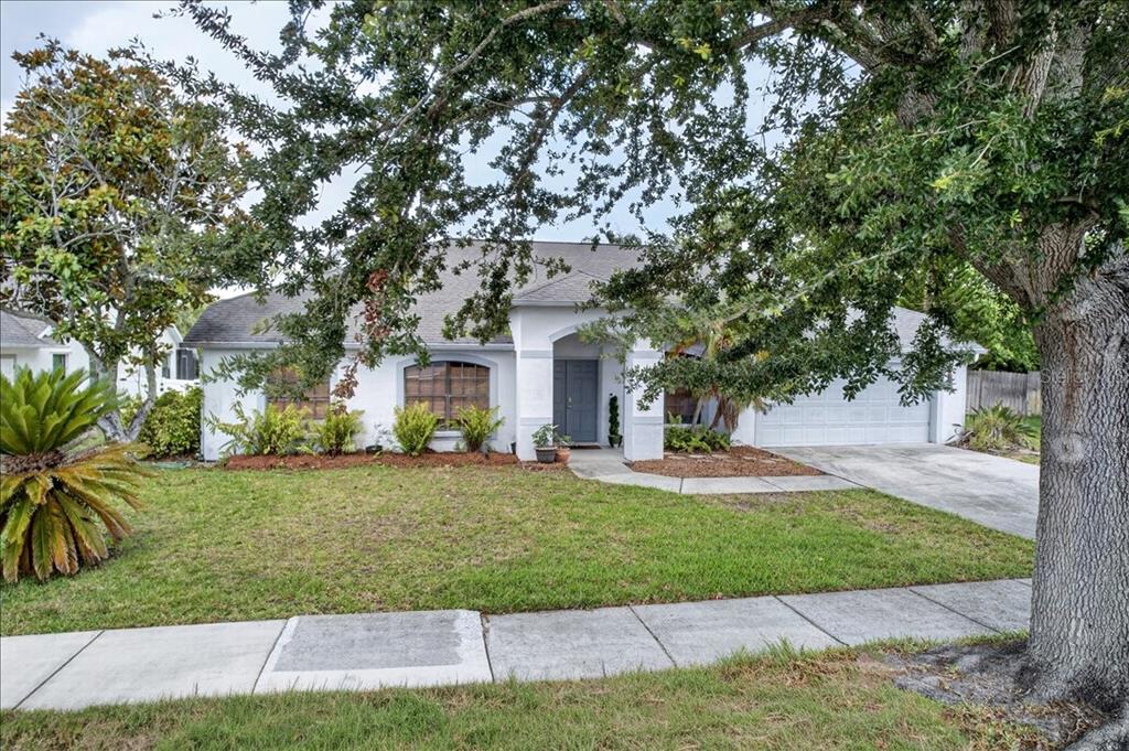 A single-story white house with a gray front door, arched entryway, and a large tree — 5068 ALAMANDA DRIVE, MELBOURNE, FL
