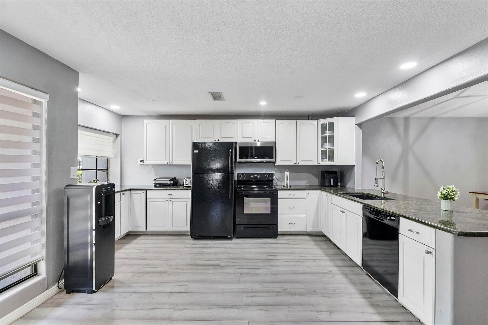 A kitchen features white cabinets, black appliances, dark countertops, and light wood-look flooring — 4149 Palm Forest Drive S, Delray Beach FL 33445, DELRAY BEACH, FL