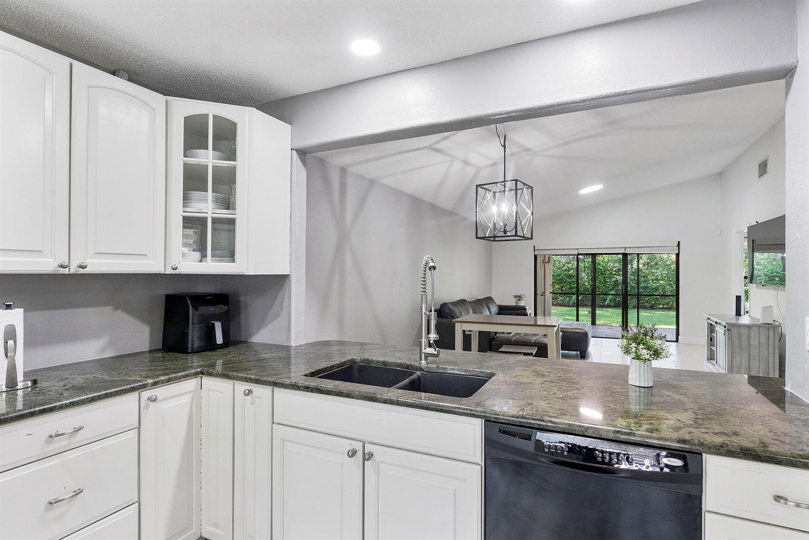 A kitchen with white cabinets and dark granite countertops overlooks a living area with sliding doors — 4149 Palm Forest Drive S, Delray Beach FL 33445, DELRAY BEACH, FL