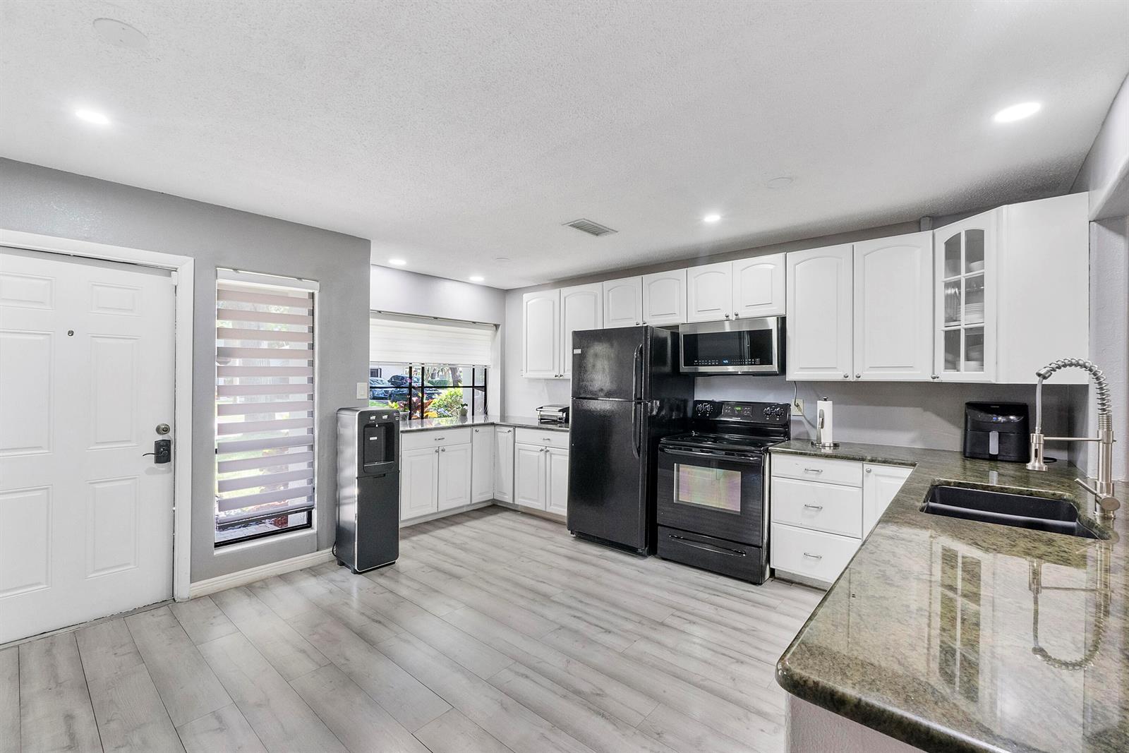 A kitchen features white cabinets, black appliances, granite countertops, and light wood-look flooring — 4149 Palm Forest Drive S, Delray Beach FL 33445, DELRAY BEACH, FL