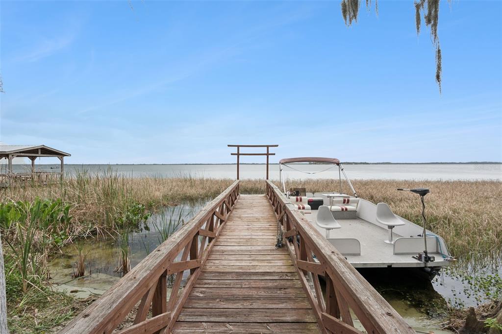 A wooden dock extends into a lake with a pontoon boat moored alongside — 35312 W GRIFFIN DRIVE, FRUITLAND PARK, FL