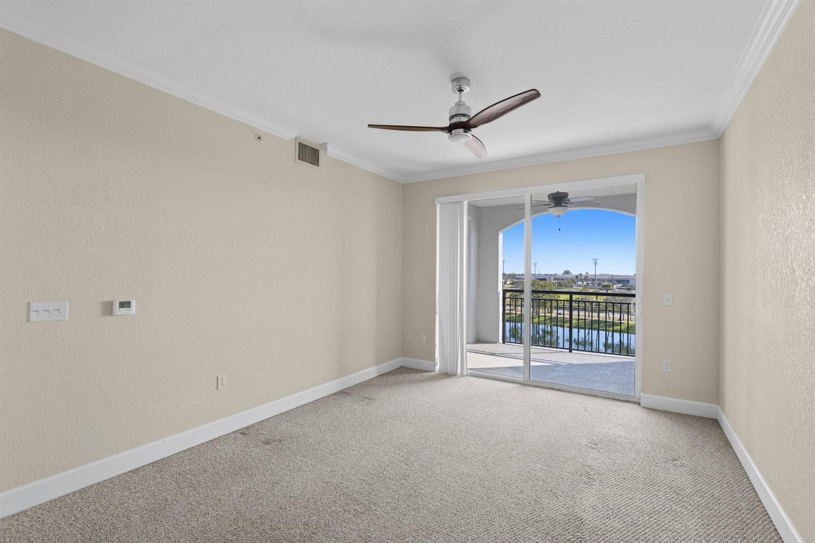 An empty bedroom features beige walls, carpeted flooring, a ceiling fan, and a sliding glass door — 1660 Renaissance Commons Boulevard # 2510, Boynton Beach FL 33426, BOYNTON BEACH, FL