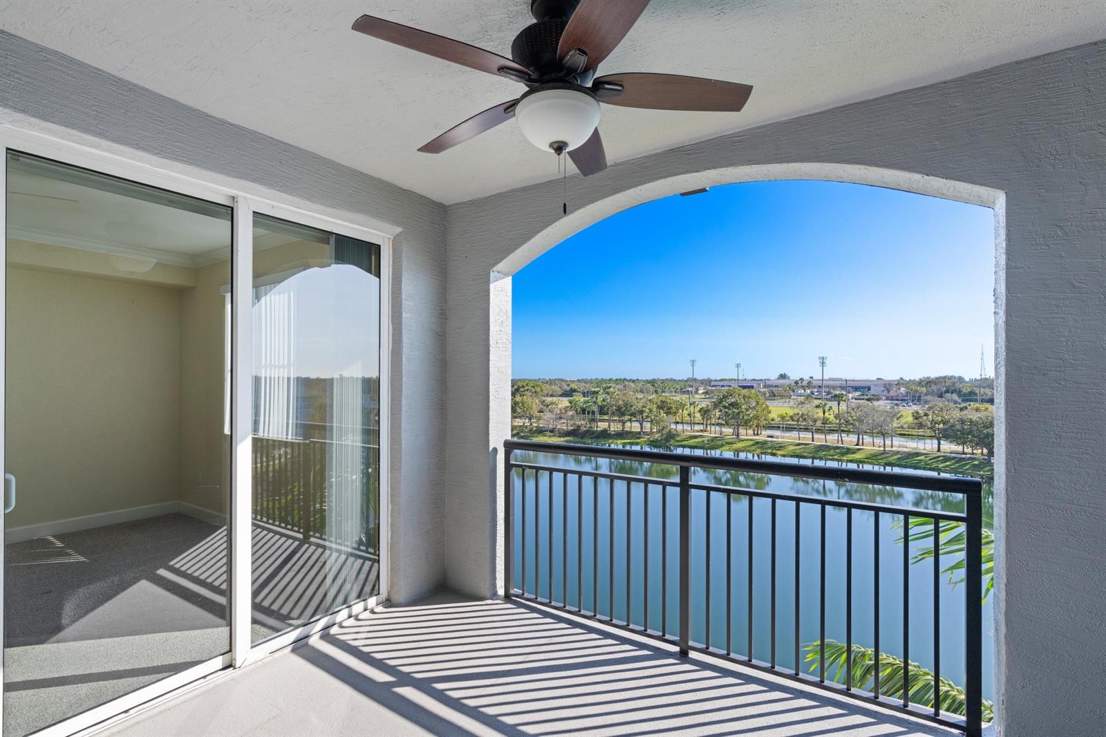 A covered balcony with a ceiling fan overlooks a lake and a distant landscape — 1660 Renaissance Commons Boulevard # 2510, Boynton Beach FL 33426, BOYNTON BEACH, FL