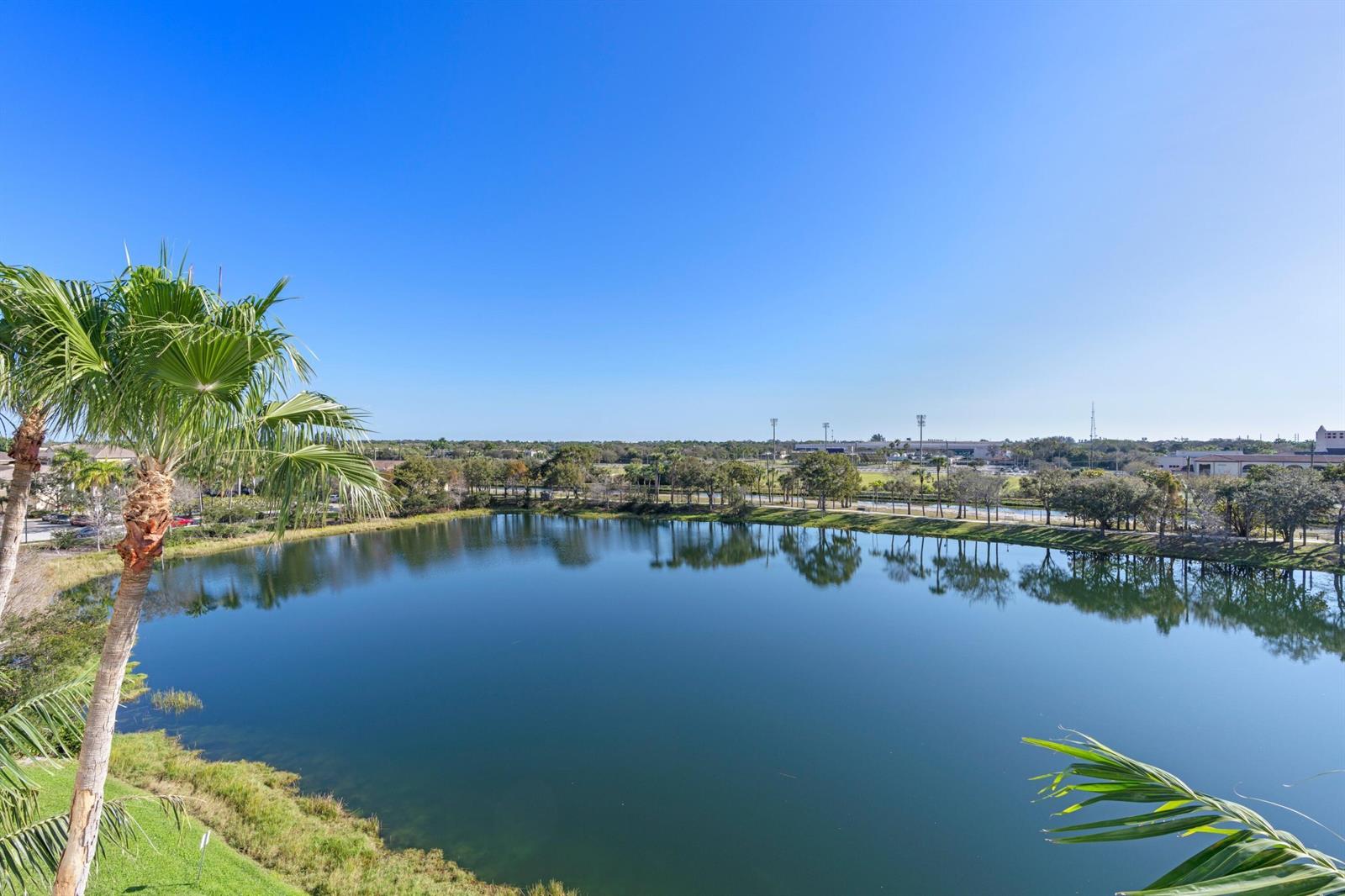 A view of a calm lake surrounded by trees under a clear blue sky — 1660 Renaissance Commons Boulevard # 2510, Boynton Beach FL 33426, BOYNTON BEACH, FL