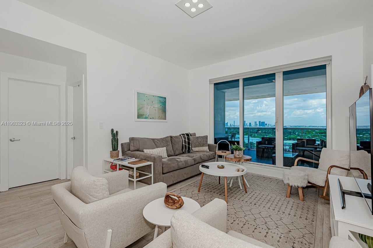 A living room features a gray sofa, white armchairs, and a balcony with city views — 2301 Collins Ave, Miami Beach FL 33139, MIAMI BEACH, FL