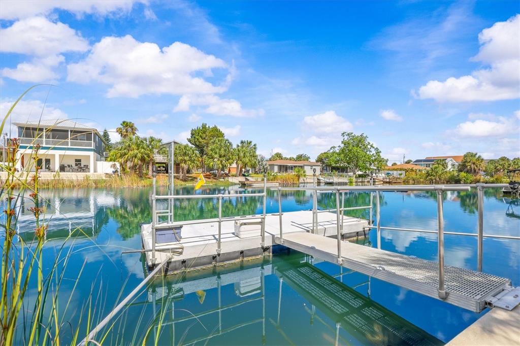A metal floating dock extends into a calm canal surrounded by houses and palm trees — 3305 ROSE ARBOR DRIVE, HERNANDO BEACH, FL