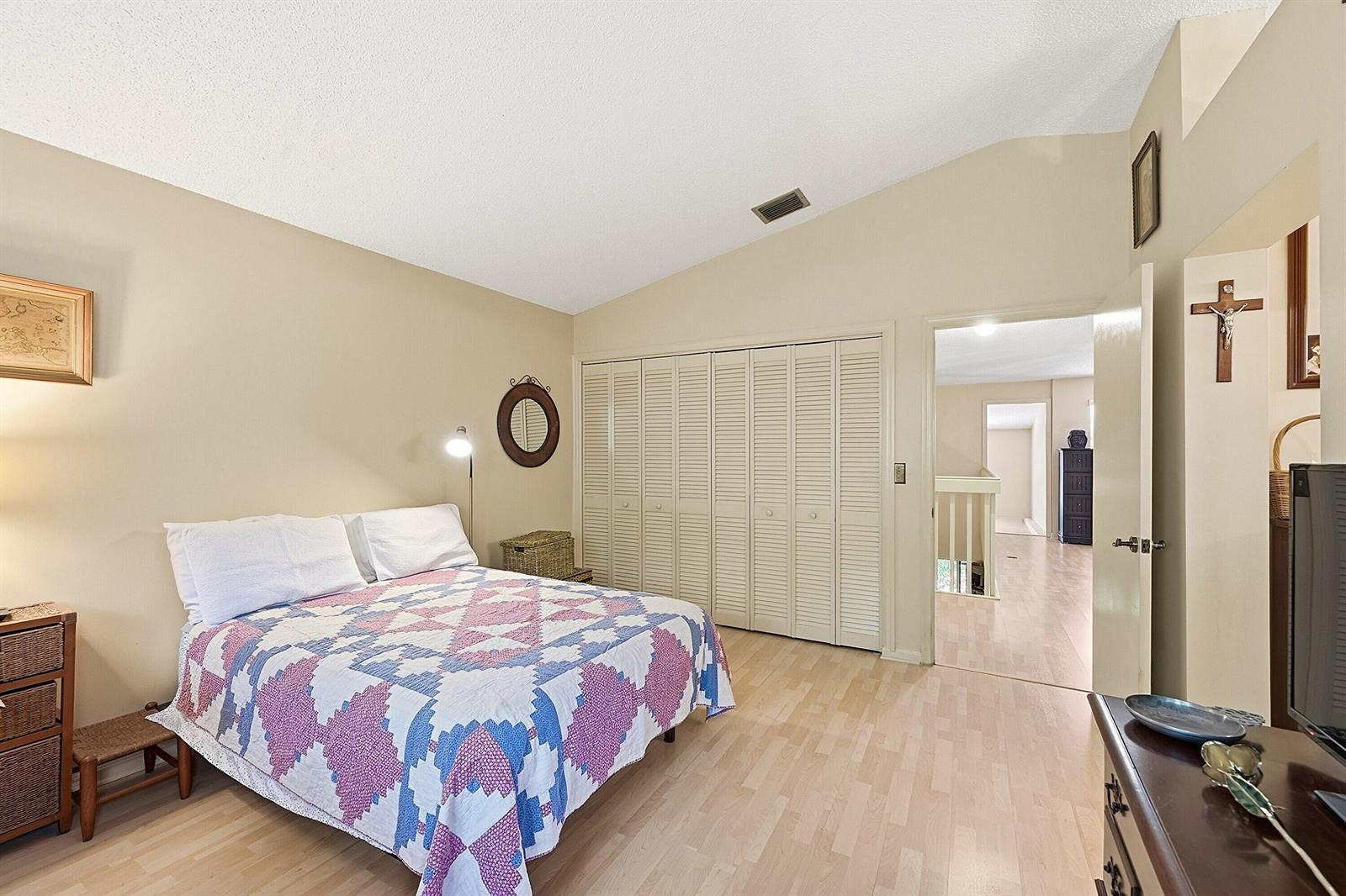 A bedroom with a vaulted ceiling, light wood flooring, a quilt-covered bed, and closet doors — 2118 Discovery Circle W, Deerfield Beach FL 33442, DEERFIELD BEACH, FL