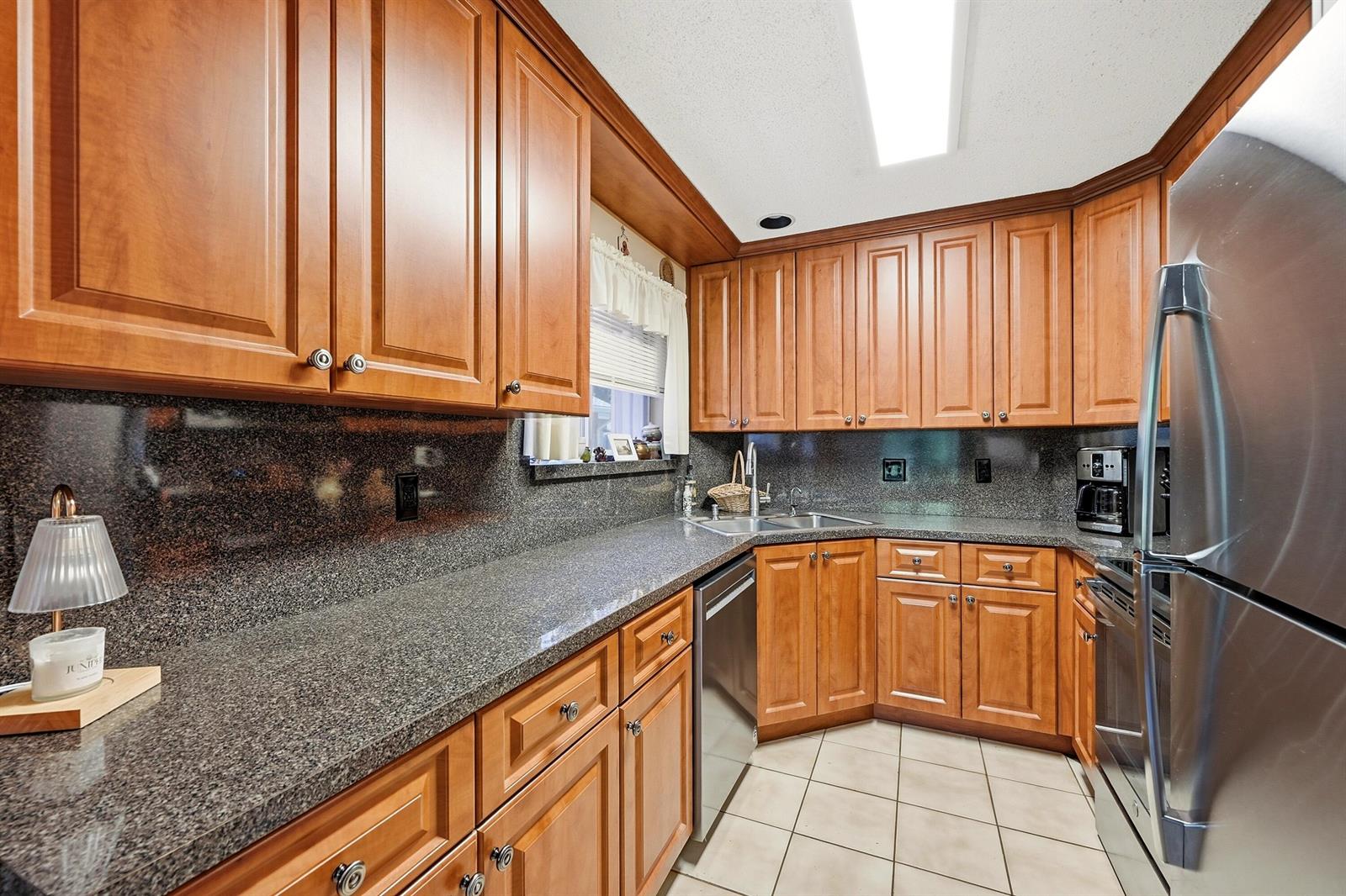 A kitchen features wood cabinets, dark granite countertops, stainless steel appliances, and tile flooring — 2118 Discovery Circle W, Deerfield Beach FL 33442, DEERFIELD BEACH, FL