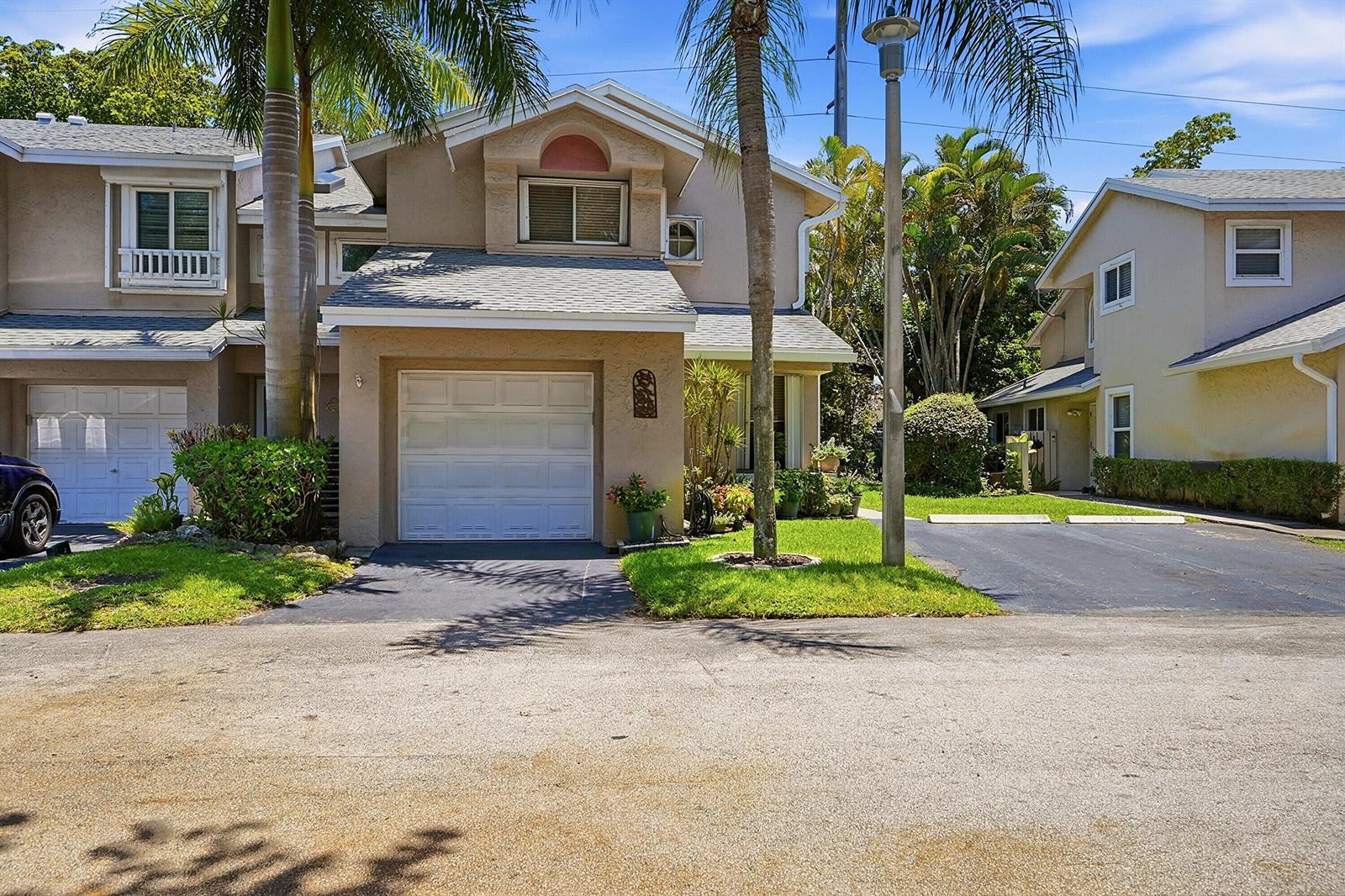 A two-story townhouse with a beige stucco exterior, a single-car garage, and palm trees — 2118 Discovery Circle W, Deerfield Beach FL 33442, DEERFIELD BEACH, FL