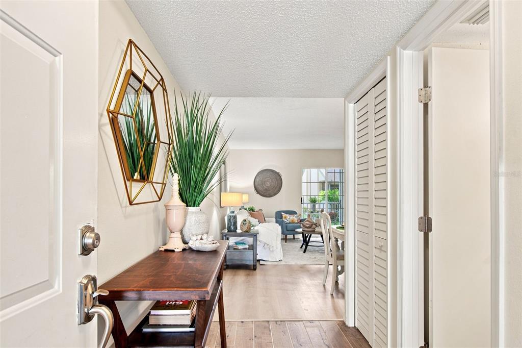 An entryway with a wooden console table and geometric mirror leads into a living area — 4701 DUHME ROAD UNIT 1D, MADEIRA BEACH, FL