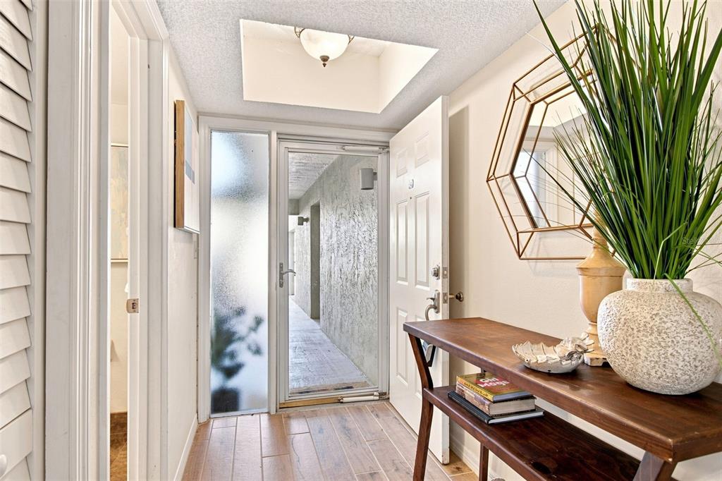 An entryway features a wood console table, a decorative mirror, and a glass-paneled front door — 4701 DUHME ROAD UNIT 1D, MADEIRA BEACH, FL