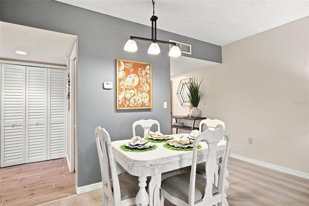 A dining room features a white table, four chairs, and a modern three-light pendant fixture — 4701 DUHME ROAD UNIT 1D, MADEIRA BEACH, FL