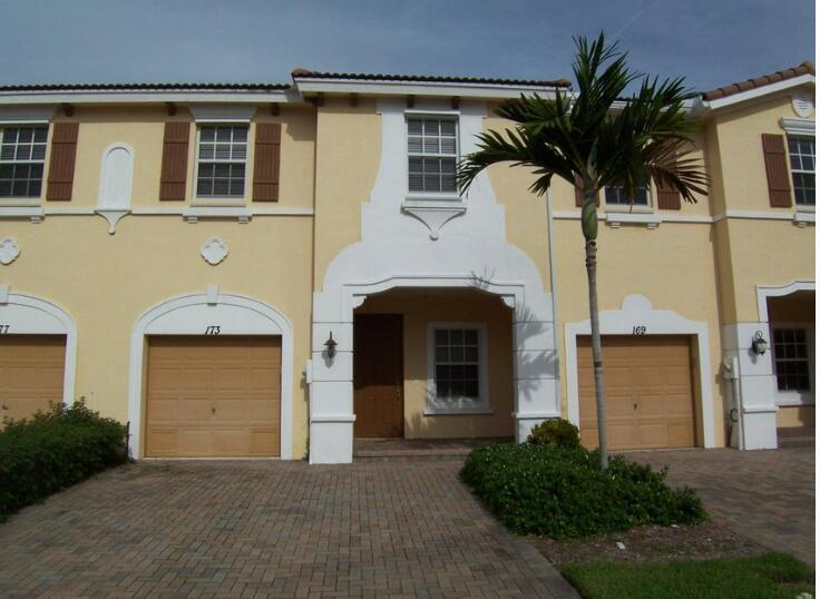 A two-story townhouse exterior with a tan stucco facade, brown garage doors, and a palm tree — 173 SW Otter Run Place, Stuart FL 34997, STUART, FL