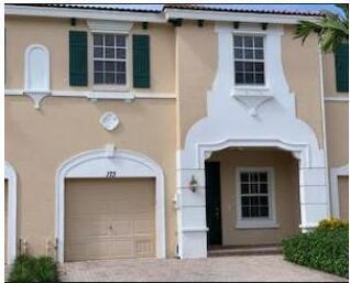 A two-story tan townhouse with a single-car garage, dark green shutters, and a covered entryway — 173 SW Otter Run Place, Stuart FL 34997, STUART, FL