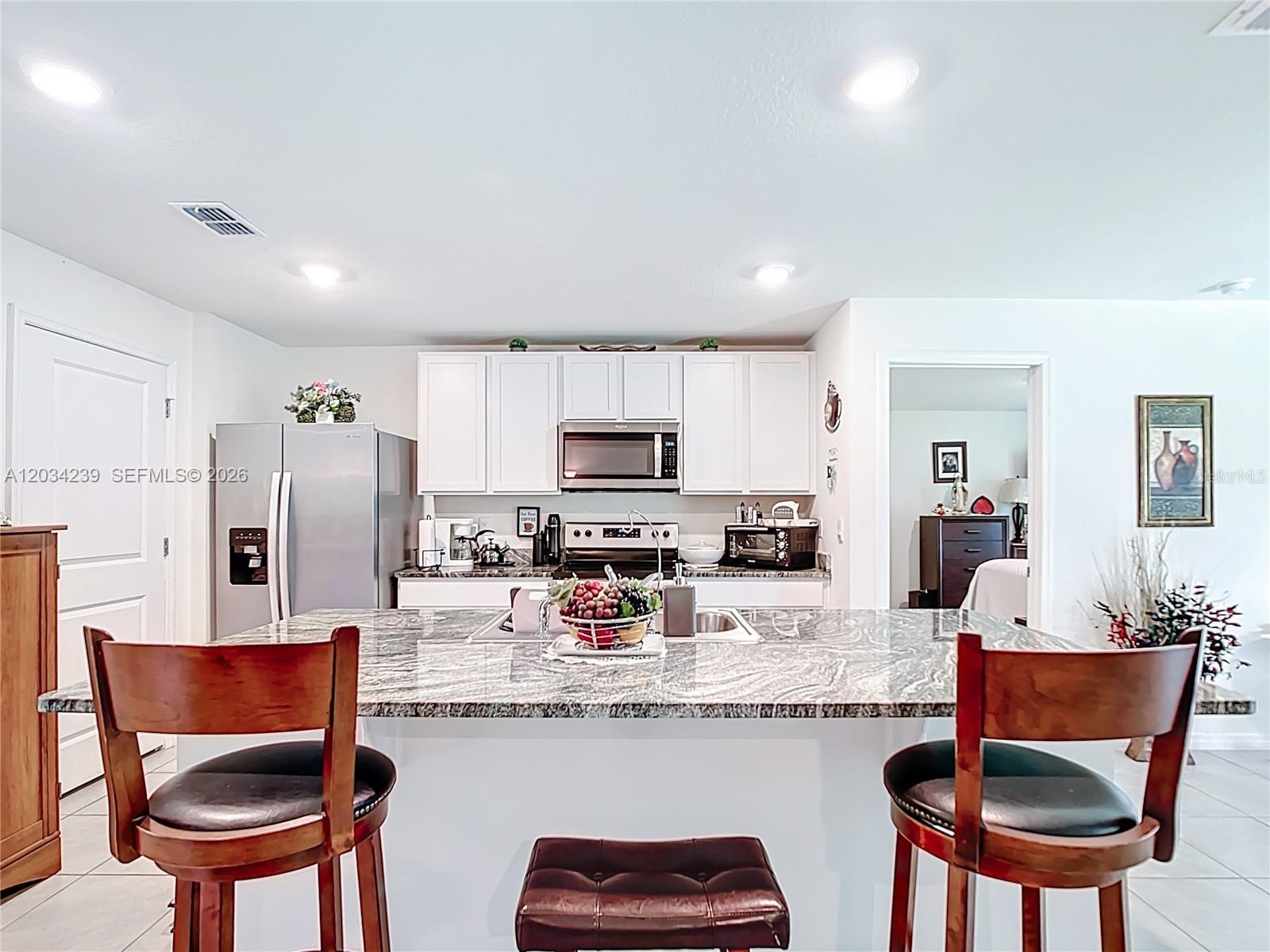 A kitchen features white cabinets, granite countertops, a central island, and two wooden bar stools — 7161 SW 135TH PLACE, Ocala FL 34473, OCALA, FL