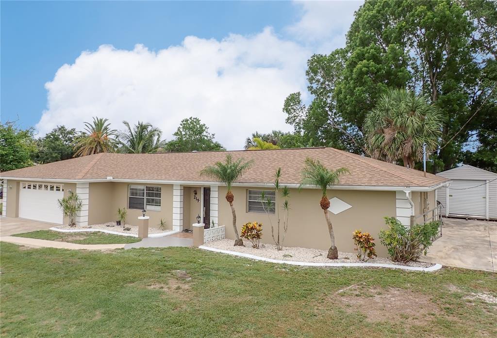 A single-story tan house with a brown shingled roof, palm trees, and a detached garage — 215 TARPON WAY, PUNTA GORDA, FL