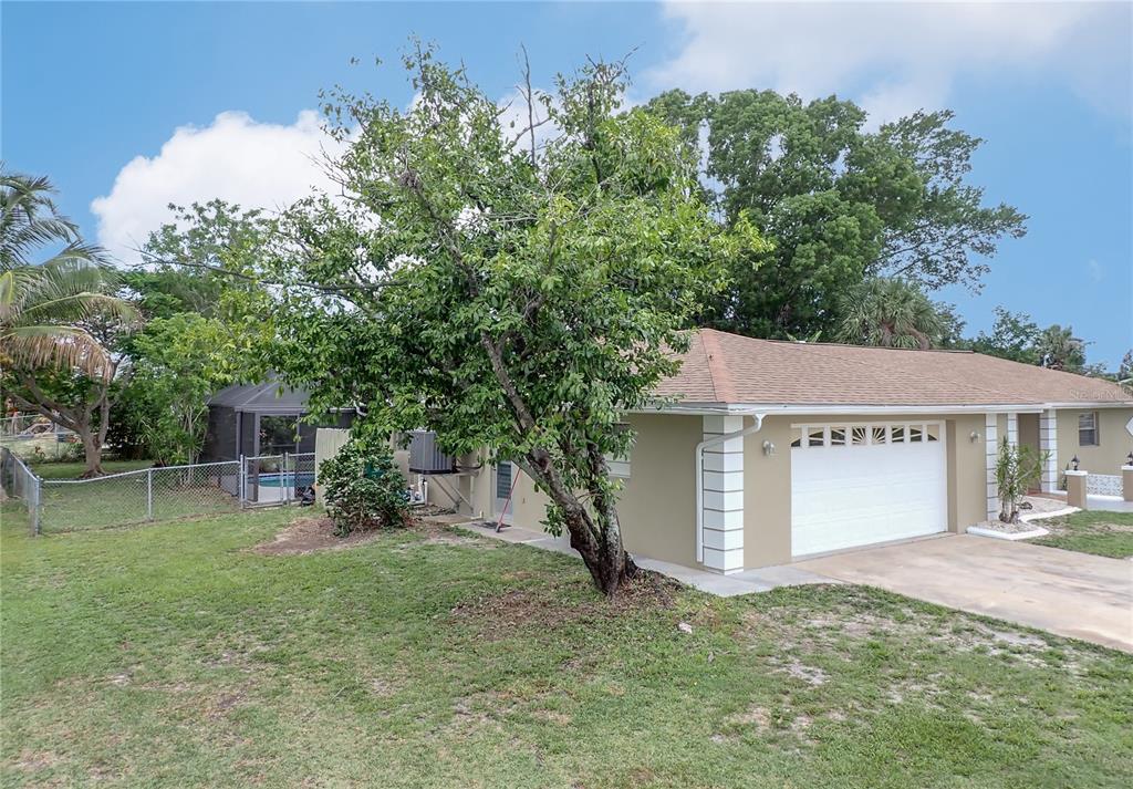 A tan house with a white garage door sits behind a large tree in a yard — 215 TARPON WAY, PUNTA GORDA, FL