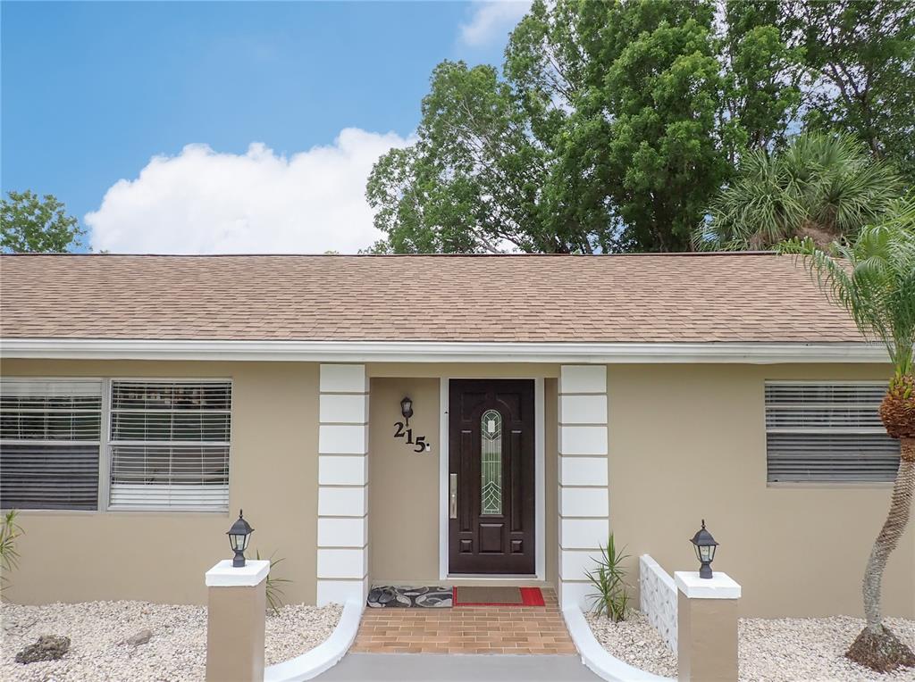 The exterior of a single-story house features a brown front door, white trim, and gravel landscaping — 215 TARPON WAY, PUNTA GORDA, FL