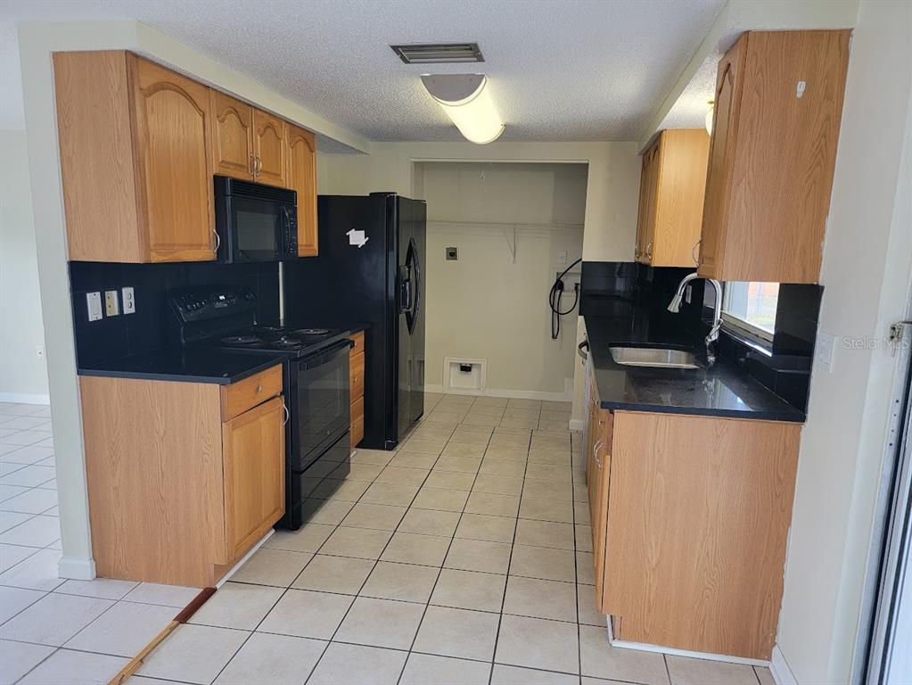 A kitchen features oak cabinets, black countertops, black appliances, and light-colored tile flooring — 22353 BUFFALO AVENUE, PORT CHARLOTTE, FL