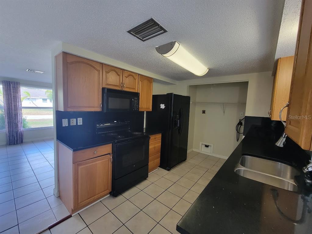 A kitchen with wooden cabinets, black appliances, black countertops, and light-colored tile flooring — 22353 BUFFALO AVENUE, PORT CHARLOTTE, FL