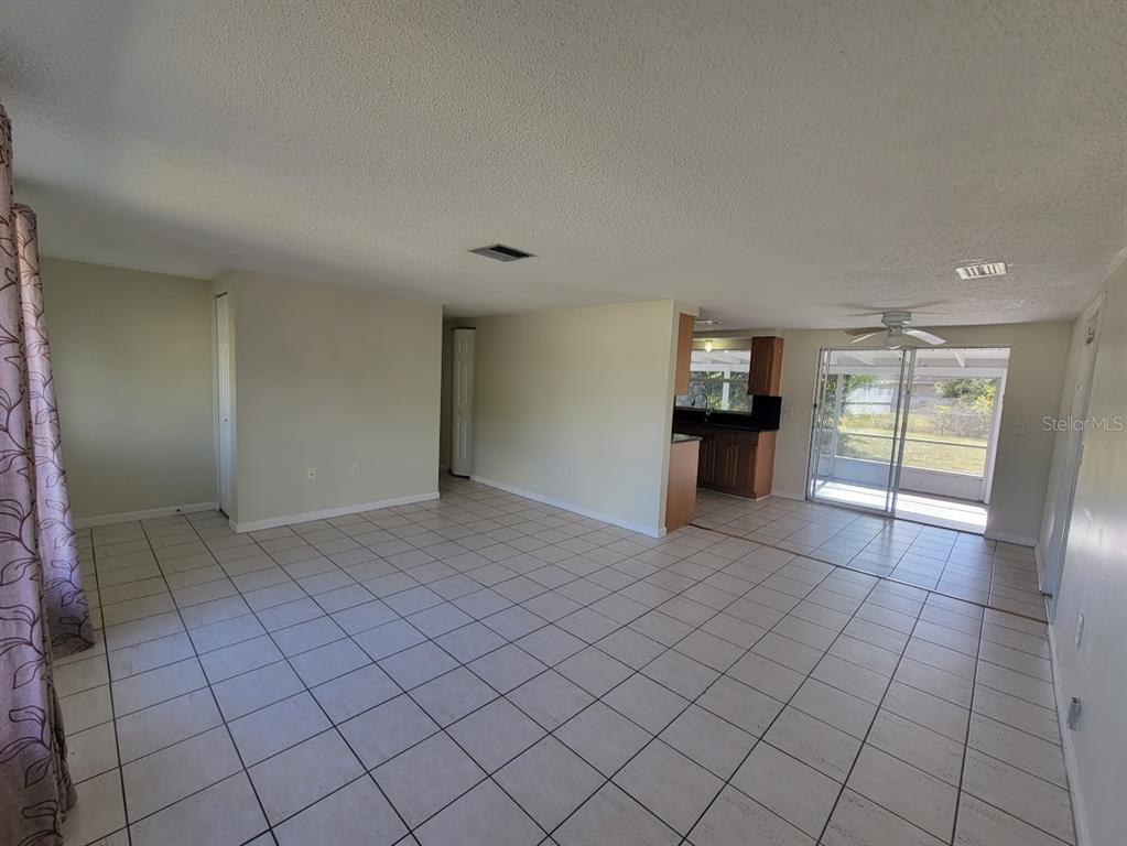 An open-concept living area features light-colored floor tiles, beige walls, and a sliding glass door — 22353 BUFFALO AVENUE, PORT CHARLOTTE, FL