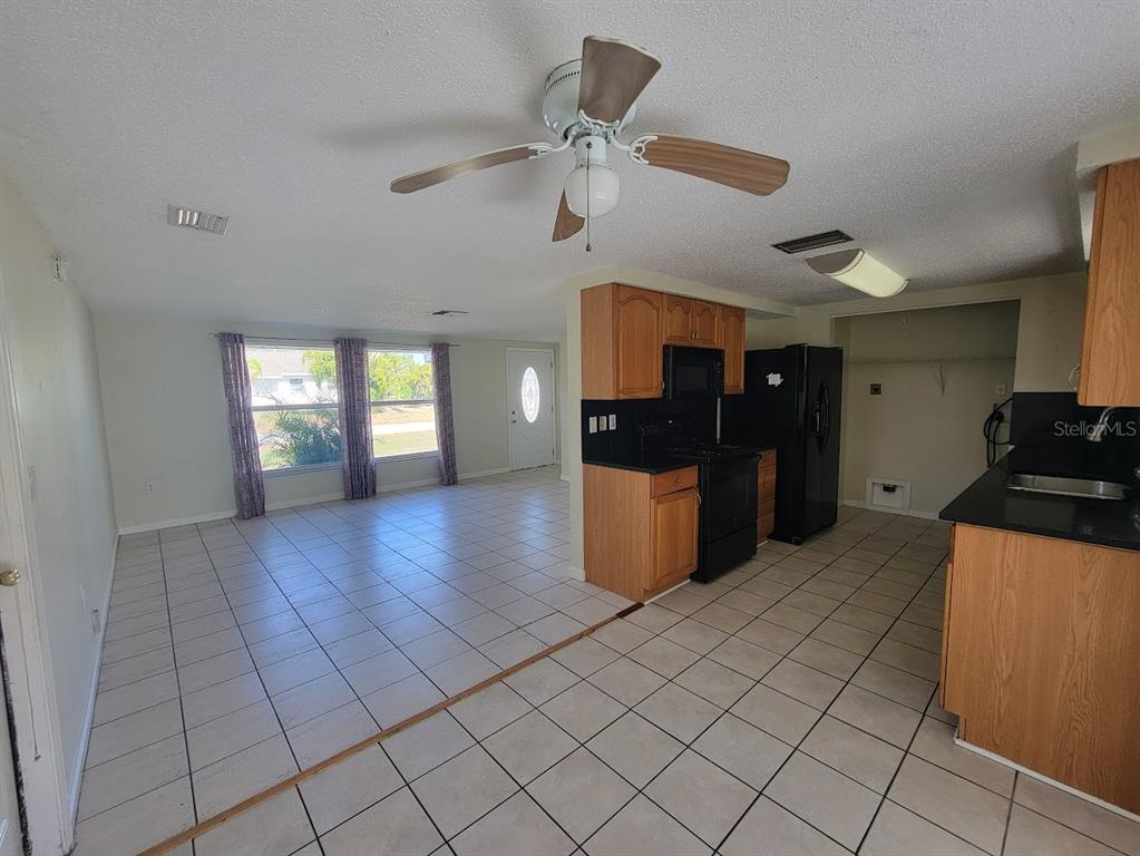 An open-concept kitchen with wood cabinets and black appliances overlooks a tiled living area — 22353 BUFFALO AVENUE, PORT CHARLOTTE, FL