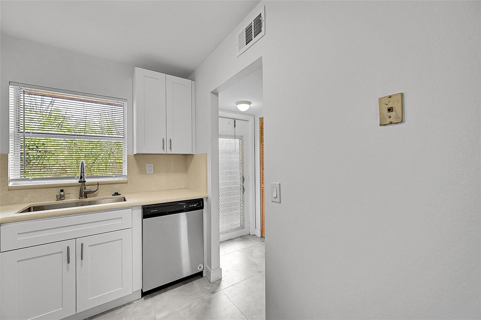 A kitchen features white cabinets, a stainless steel dishwasher, a window, and a doorway — 9761 Sunrise Lakes Boulevard # 301, Sunrise FL 33322, SUNRISE, FL