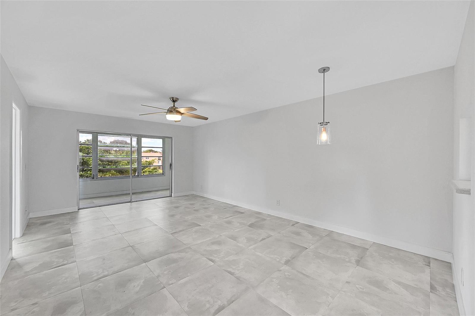 A bright, empty room features large light-gray floor tiles, a ceiling fan, and sliding glass doors — 9761 Sunrise Lakes Boulevard # 301, Sunrise FL 33322, SUNRISE, FL