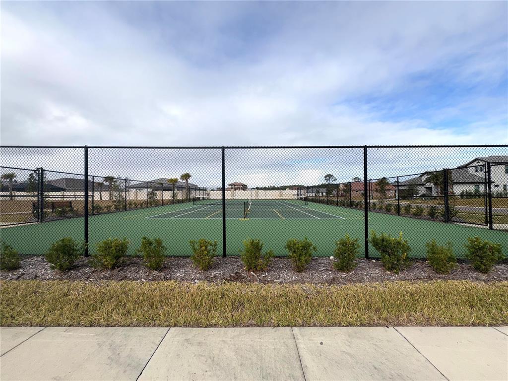 A fenced-in outdoor tennis court sits behind a row of small shrubs and grass — 48 DEL PALMA DRIVE, PALM COAST, FL