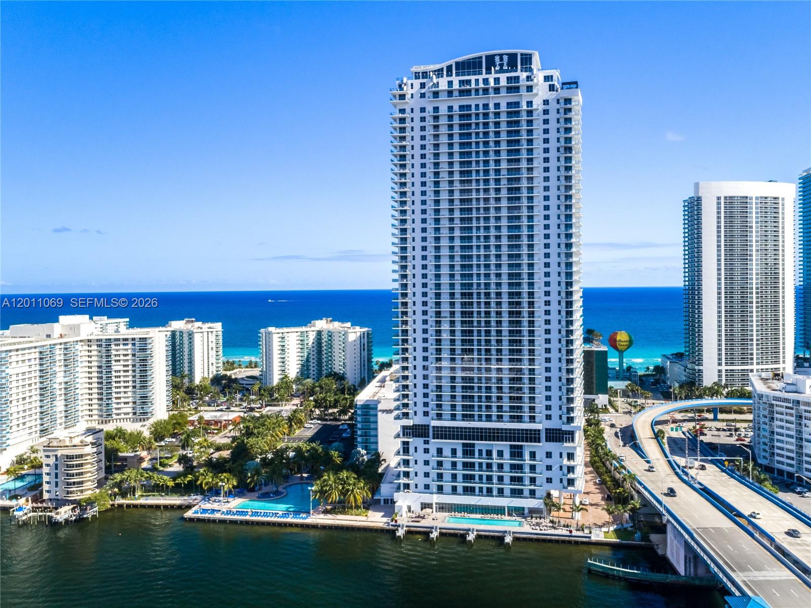 An aerial view shows a tall white residential tower beside a waterway and highway — 4010 S Ocean Dr # R908, Hollywood FL 33019, HOLLYWOOD, FL