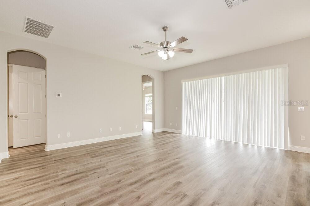 An empty living room features light wood-look flooring, a ceiling fan, and sliding glass doors — 1174 GREEN VISTA CIRCLE, APOPKA, FL