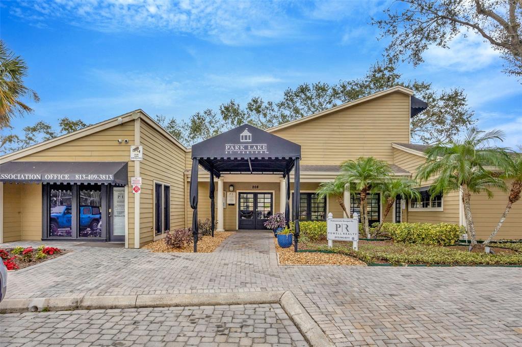 The exterior of a tan building features a central entrance with a black fabric awning — 308 LAKE PARSONS GREEN UNIT 102, BRANDON, FL