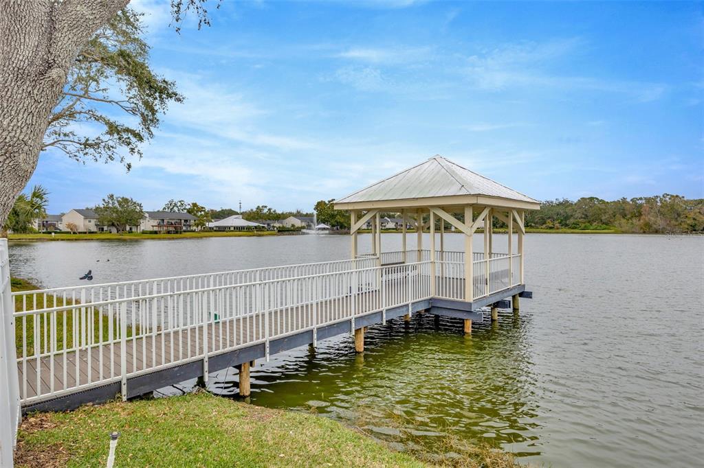 A wooden pier with a covered gazebo extends into a lake near residential buildings — 308 LAKE PARSONS GREEN UNIT 102, BRANDON, FL