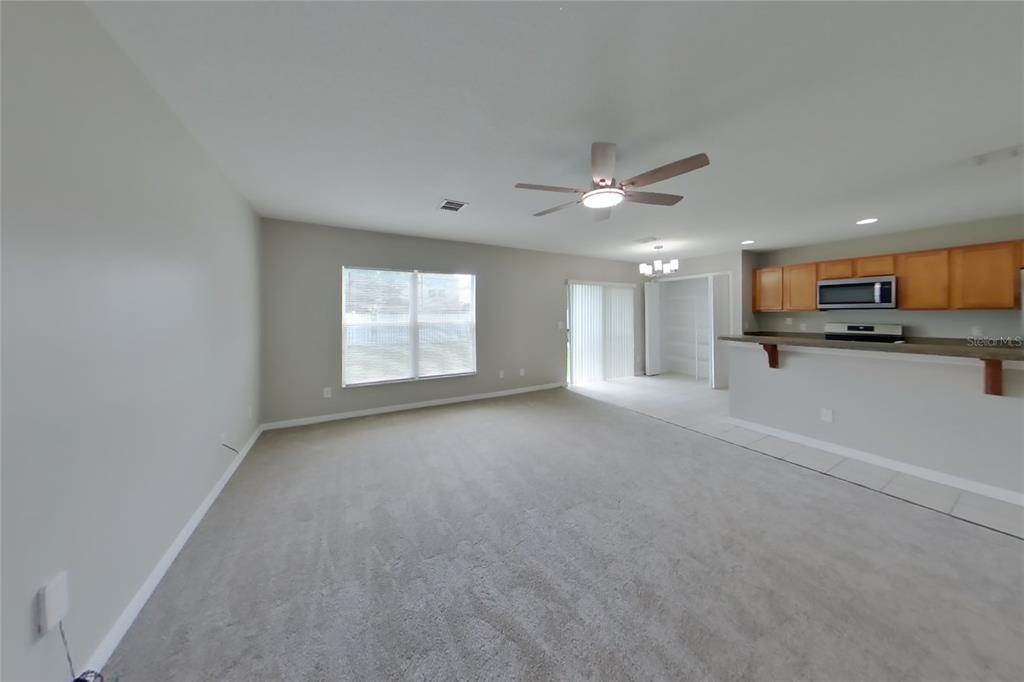 A living room with beige carpet, a ceiling fan, and an adjacent kitchen with cabinets — 1708 PORTCASTLE CIRCLE, WINTER GARDEN, FL
