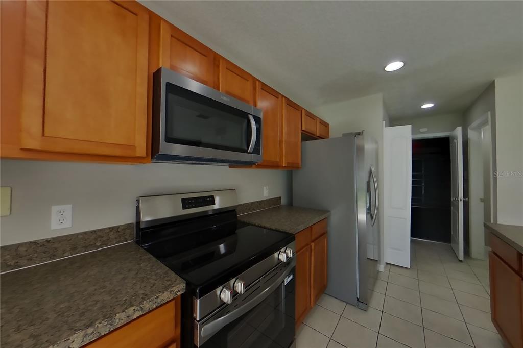 A kitchen features wood cabinets, stainless steel appliances, and dark countertops — 1708 PORTCASTLE CIRCLE, WINTER GARDEN, FL